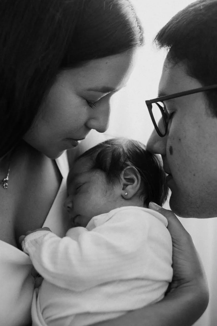 Pais beijando o recém-nascido, em preto e branco